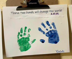 A piece of art by a preschooler named Violet. It features two of her handprints - the left green, the right blue. At the top a teacher has written, 